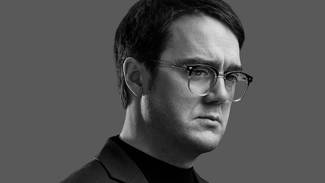 Photo en noir et blanc d'un homme qui porte des lunettes. 