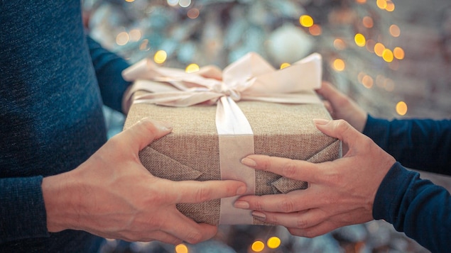 Un homme et une femme s'échangent un cadeau devant un sapin de Noël. 