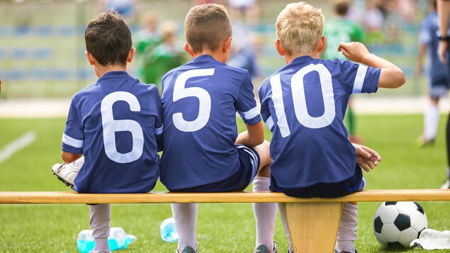 Trois jeunes joueurs de soccer de dos, assis sur un banc.