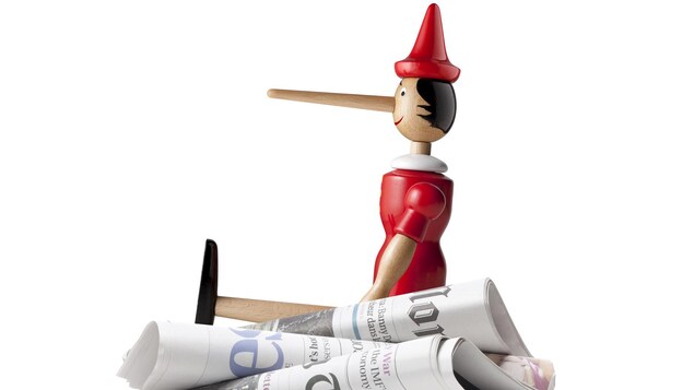 Un Pinocchio assis sur une pile de journaux pour représenté les Fake News.