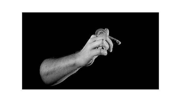 Un tableau en noir et blanc montre une main d'homme qui tient une pièce de monnaie entre les doigts