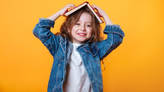 Une petite fille rieuse a posé un livre sur sa tête.