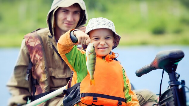 Un garçon souriant dans une chaloupe tient un poisson qu'il vient de pêcher.