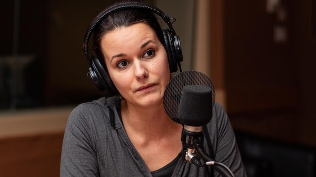 La journaliste, casque d'écoute sur la tête, est derrière un micro dans un studio de radio.