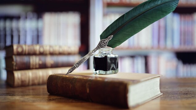 Une plume et un encrier sont posés sur un vieux livre sur une table.