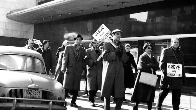 À l'extérieur, lors de la grève des réalisateurs
de Radio-Canada en 1958-1959, des
réalisateurs avec des pancartes défilent
devant l'Édifice Radio-Canada, dont Rolland
Guay à l'avant et Pierre Desroches à
l'extrême-droite.