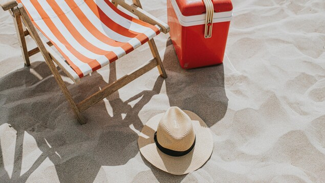 Un chapeau de paille, une glacière et une chaise de plage sur une plage de sable fin. 