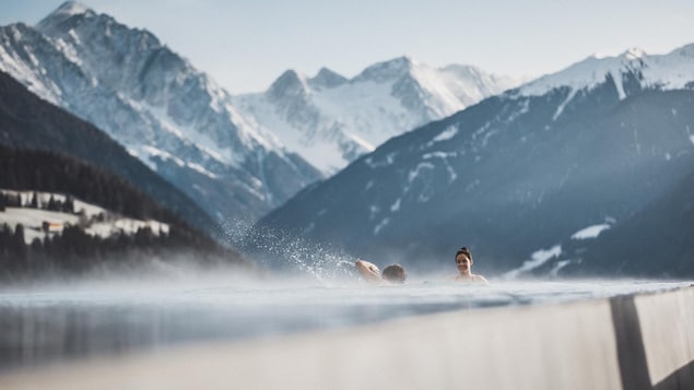 Un couple dans une piscine chauffée avec des montagnes derrière.
