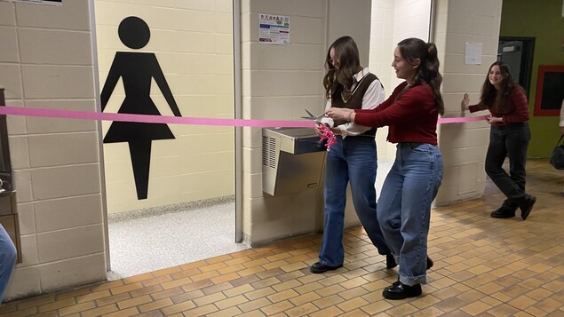 Des jeunes femmes coupent un ruban rose devant les toilettes. 