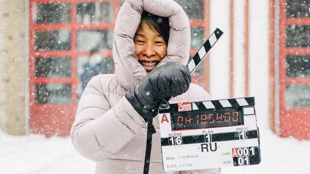 Une femme (Kim Thúy) souriante, sous la neige, tient un clap de cinéma.