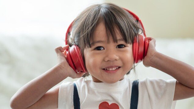 Une petite fille asiatique sourit en portant un casque audio