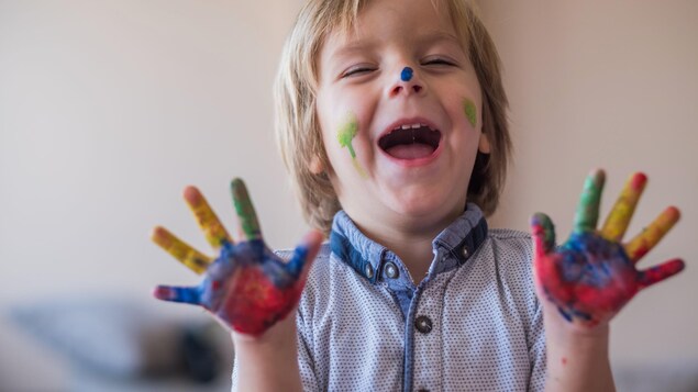 Le petit garçon d'environ 4 ans rit en montrant ses mains pleines de peinture