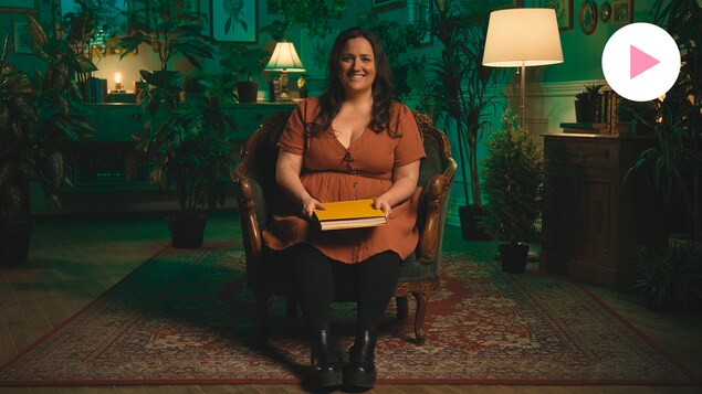 Caroline Huard alias Loounie est assise dans un fauteuil sur un tapis dans une pièce entourée de plantes et de tableaux botaniques.