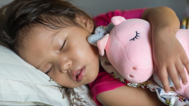 Une fillette dort en tenant une peluche licorne