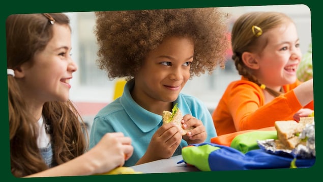 Deux petites filles et un petit garçon rient en mangeant leur repas. 