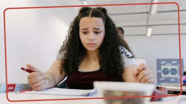 Une jeune ado est assise à sa table à l'école, l'air nerveux. 
