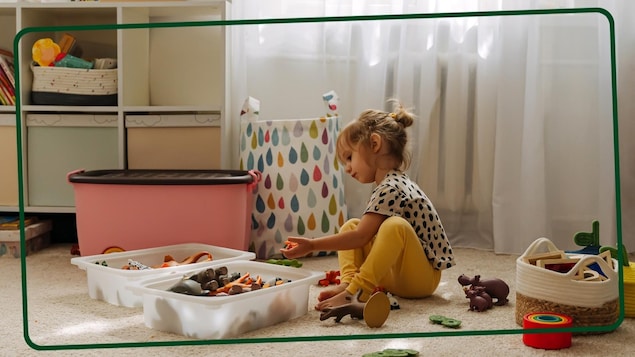 Une petite fille range ses jouets dans sa chambre. 