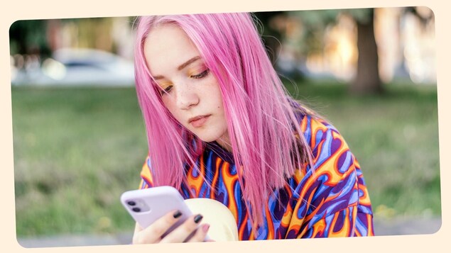 Une préado regarde son cellulaire, elle est assise dans un parc. 