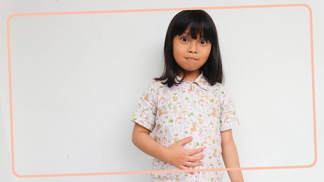 Une petite fille se touche l'estomac. 