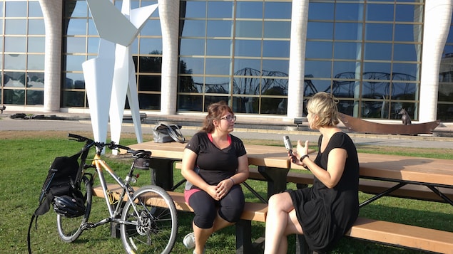 Deux femmes discutent, assises sur une table de pique-nique sur laquelle est appuyé un vélo.