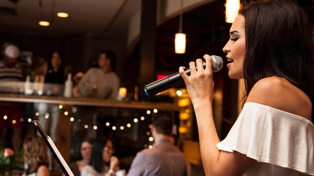 Une jeune femme vêtue de blanc chante en tenant fermement un micro.