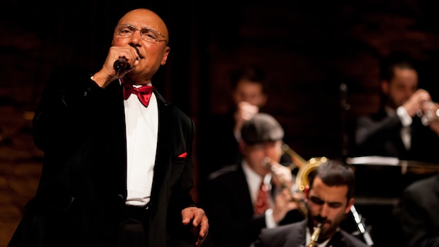 Colin Hunter en concert au Festival de jazz de Québec. On l'aperçoit en smoking, au micro devant un orchestre.