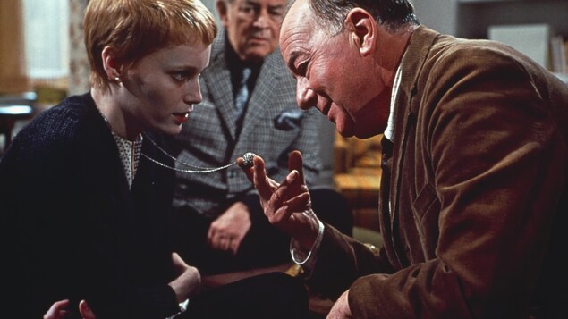 Un homme regarde le pendentif d'une jeune fille, en le tenant entre ses mains