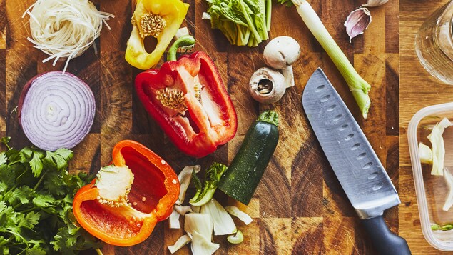 Plusieurs légumes tranchés avec un couteau de chef sur une planche à découper en bois.