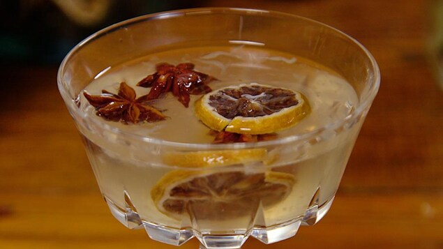 Une ponce de gin garnie d'anis étoilé et de tranches d'orange et servie dans un verre sur pied.