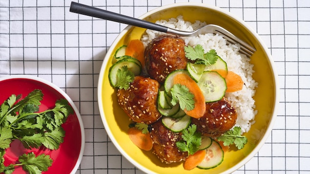 Des boulettes de porc au sésame servies avec du riz dans un bol creux, accompagnées d'une salade de concombre et carottes.