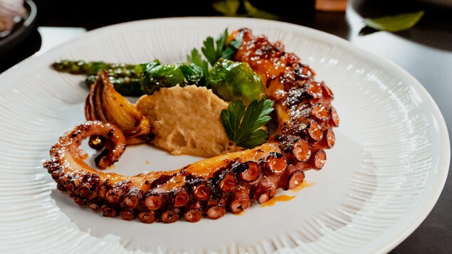 Un tentacule de pieuvre laquée dans une assiette avec des légumes verts et de la purée de châtaignes.