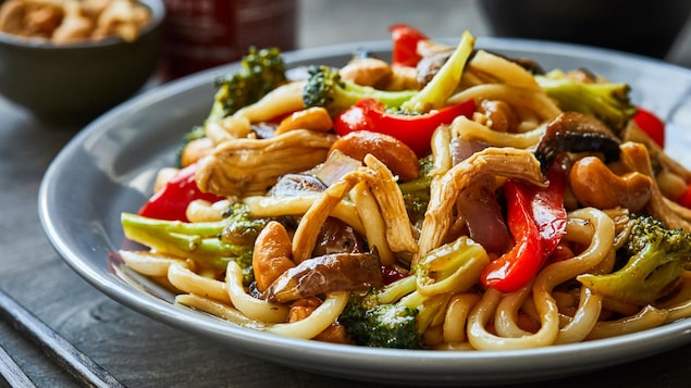 Sauté de nouilles udon au poulet effiloché dans une assiette.