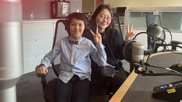 Une femme et son fils lèvent les doigts en signe de paix assis devant des micros de radio.