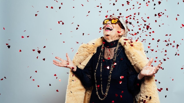 Une femme âgée avec des vêtements à la mode rigole à travers une explosion de confettis.