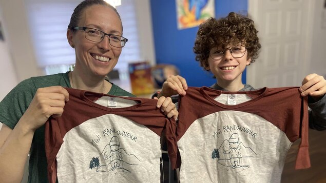 Une mère et son fils dévoilent un t-shirt sur lequel on peut lire « Mini randonneur »