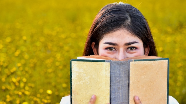 Une femme tient un livre collé sur son visage.