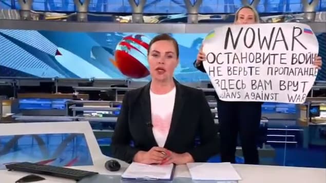 Une femme qui a surgi sur un plateau de télévision tient une pancarte disant : 
« Non à la guerre. Ne croyez pas la propagande. On vous ment, ici », derrière une lectrice de nouvelles. 