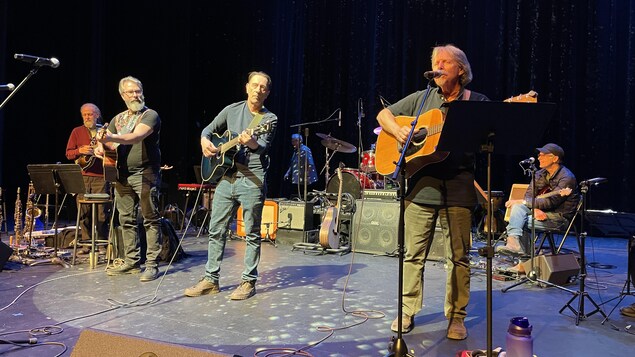 Quatre hommes sur scène avec des guitares.