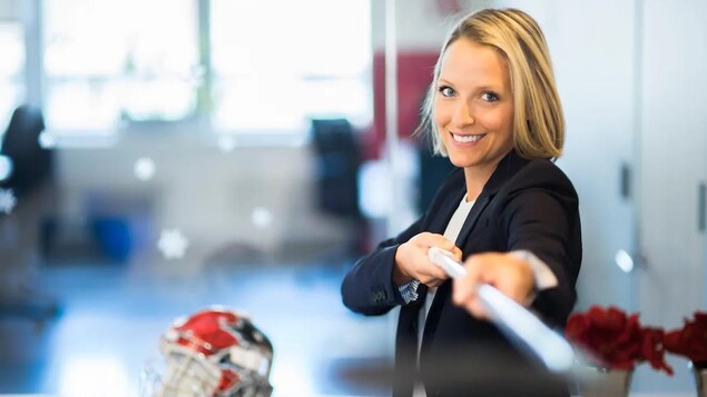 Émilie Castonguay souriant à la caméra. Elle porte un veston et tient un bâton qu'elle pointe vers la caméra.