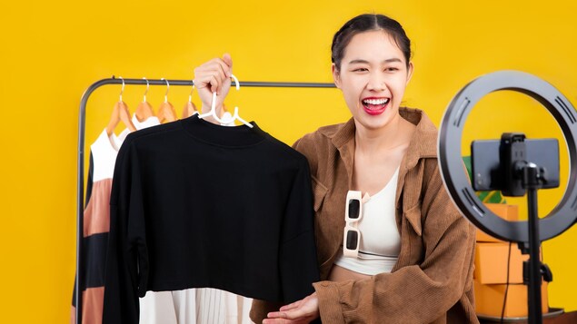 Une influenceuse présente des vêtements à vendre devant sa caméra. 