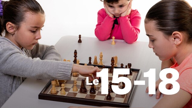 Deux jeunes filles jouent aux échecs, alors qu'une troisième les regarde.