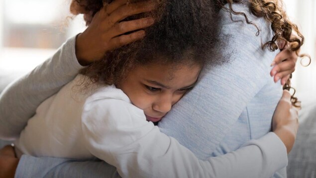 Une mère et sa fille assises sur un fauteuil se serrent dans leurs bras. 