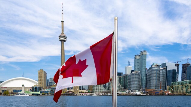 Un drapeau du Canada devant le centre-ville de Toronto, la tour CN en évidence.