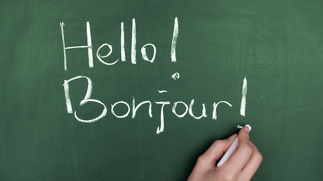 Une femme écrit « Hello! Bonjour ! » sur un tableau vert.

