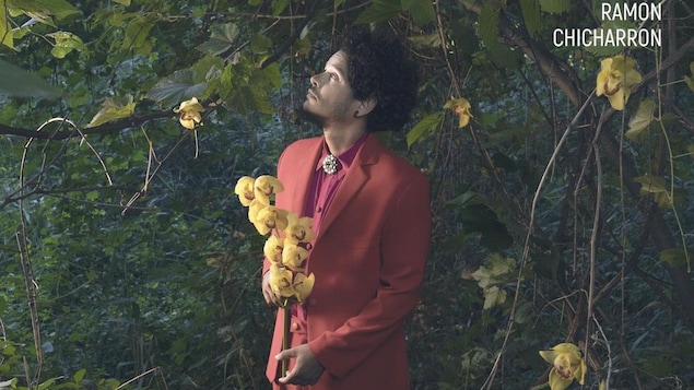 Le chanteur regarde vers le haut avec des fleurs dans la main.