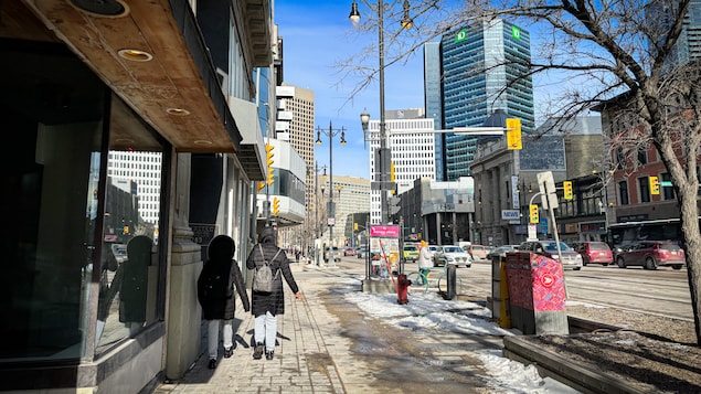 Paysage du centre-ville de Winnipeg avec deux personnes se tournant le dos et marchant dans la rue.