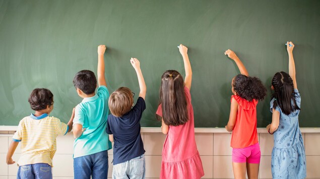 Des enfants dessinent sur un tableau avec des craies.
