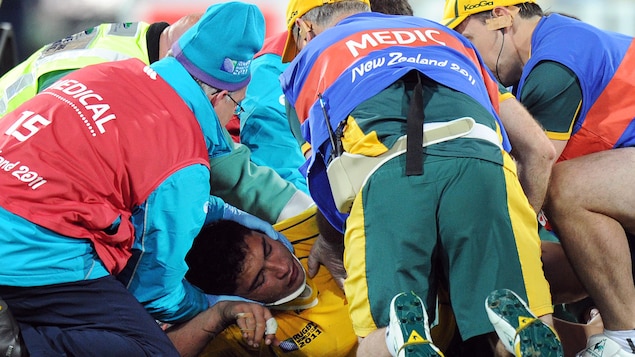 Étendu par terre, un joueur de rugby est entouré de cinq soigneurs.