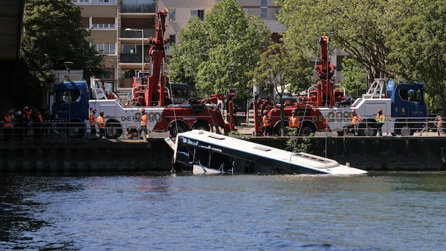 Des remorqueuses extirpent un autobus tombé dans l'eau au bord d'un quai.