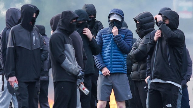 Des jeunes hommes masqués rassemblés dans une rue.